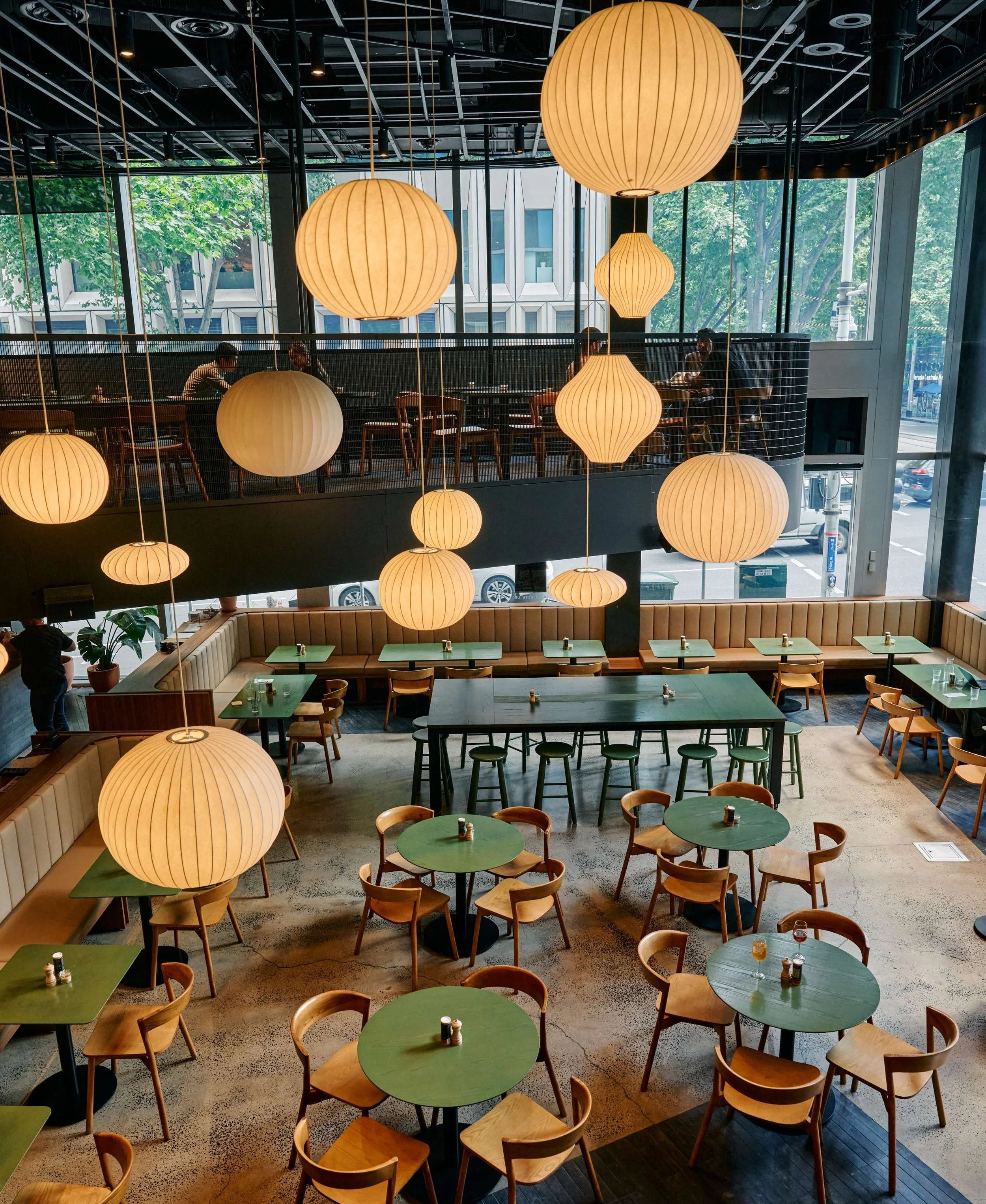 Modern restaurant interior with hanging lights and green tables.